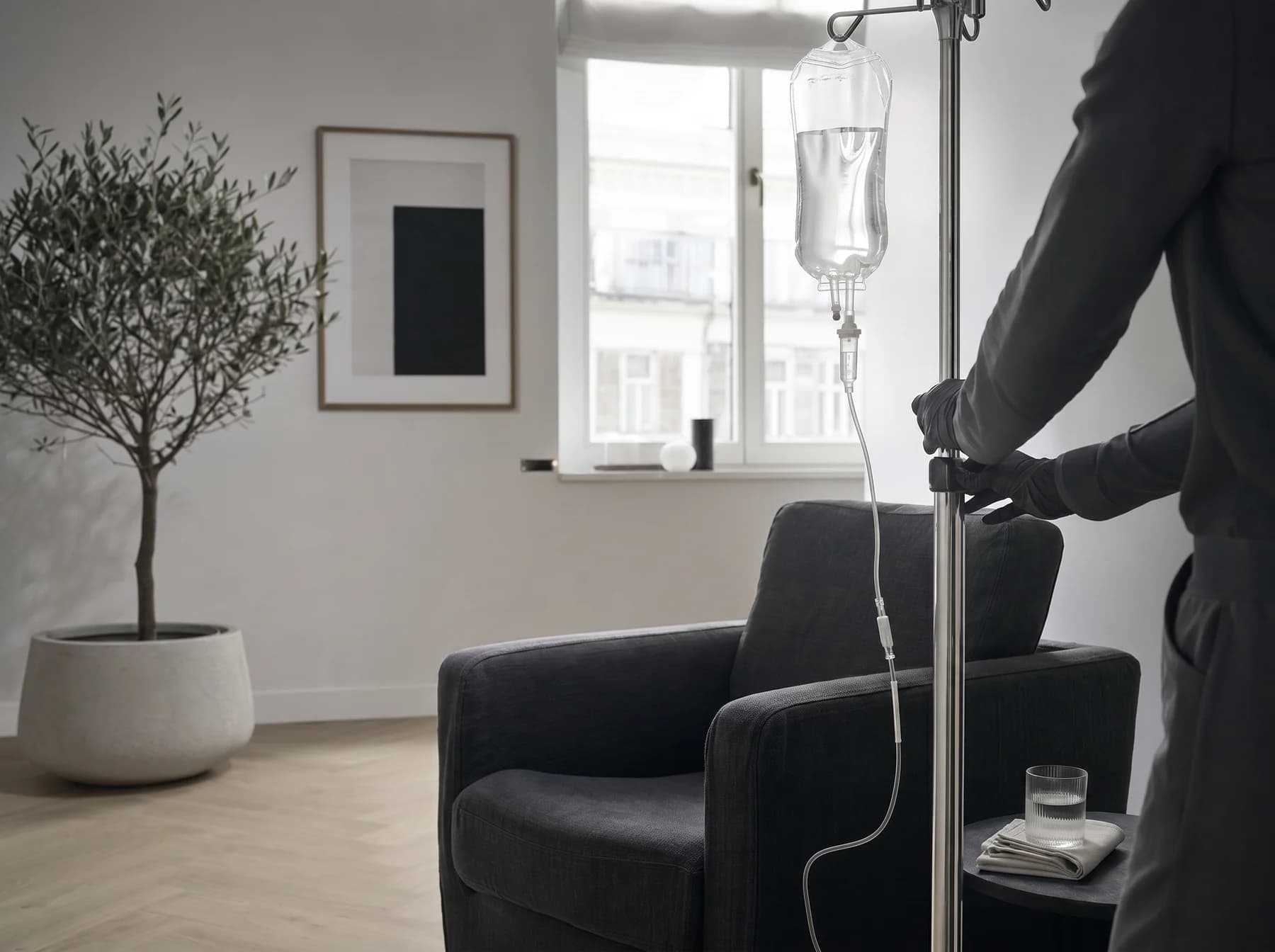 INFUZE home IV session in a Warsaw apartment — chrome IV stand beside a graphite linen chair, morning window light