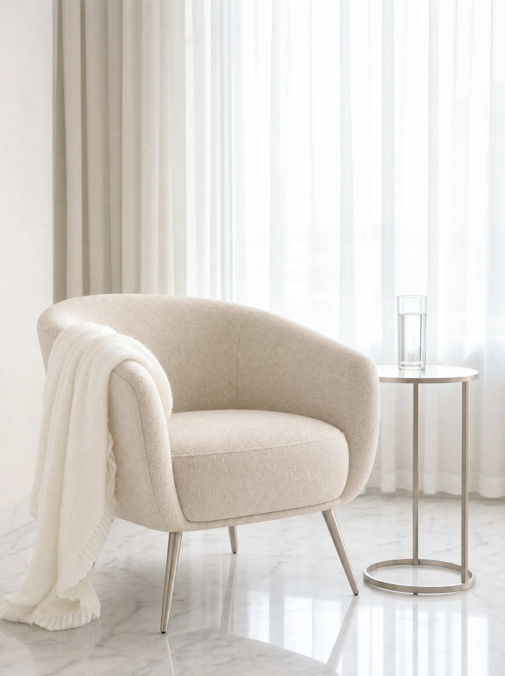 A quiet corner of an INFUZE Warsaw treatment room — a graphite linen armchair beside a tall window with cool morning light, a brushed steel side table with a single glass of water.